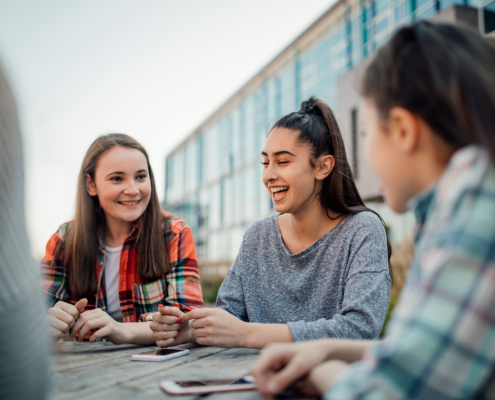 A group of schoolgirls sit talking at a table outside of school