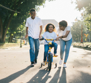 Man Standing Beside His Wife Teaching Their Child How to Ride Bicycle