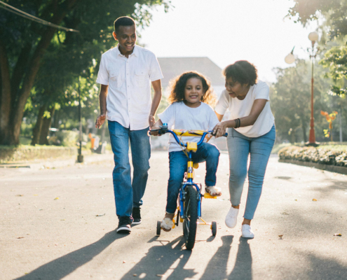 Man Standing Beside His Wife Teaching Their Child How to Ride Bicycle